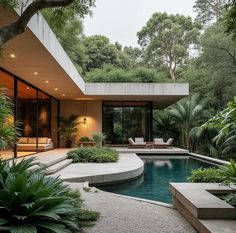 an outdoor swimming pool surrounded by greenery and trees in front of a modern house