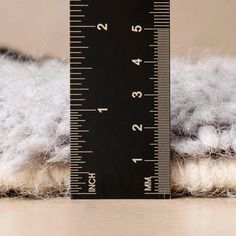 a close up of a measuring tape on top of a pile of white wool next to a ruler