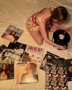 a woman laying on top of a bed covered in lots of books and magazines next to a record player