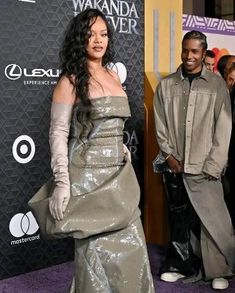 a woman in a silver dress standing next to a man on a purple carpet at an awards event