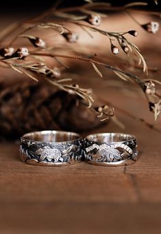 two wedding rings sitting on top of a wooden table next to some dry grass and flowers