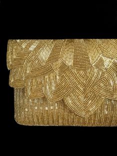 a gold clutch bag with braiding on the front and side, against a black background