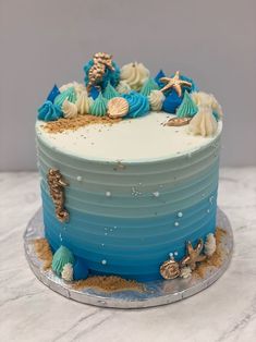 there is a blue and white cake with shells on the top, along with other decorations