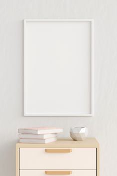 a white frame on top of a dresser next to a stack of books