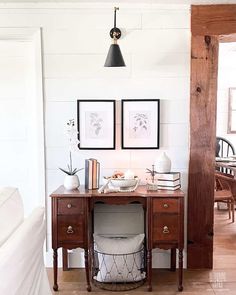 a wooden desk with two pictures on the wall and a basket underneath it in a room