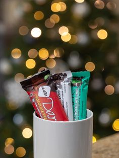 a white cup filled with candy and chocolate bars next to a christmas tree in the background