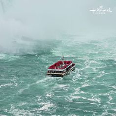 a boat filled with people on top of the ocean in front of a large waterfall