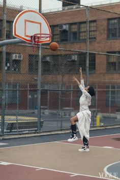 a person jumping up to dunk a basketball into the air on a court with buildings in the background