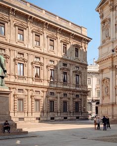 people are walking around in front of an old building with a statue on the corner