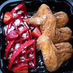 a plastic container filled with fried chicken, strawberries and powdered sugar covered waffles