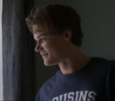 a young man looking out the window in front of a curtain with his eyes closed