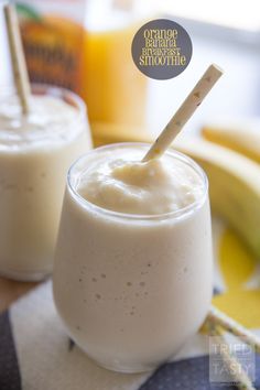 two glasses filled with smoothie sitting on top of a table next to banana slices