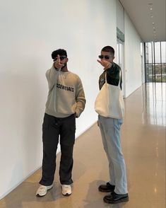 two young men standing next to each other in front of a white wall with windows