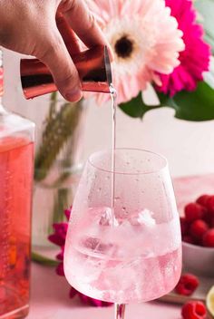 someone pouring water into a wine glass with raspberries in the background