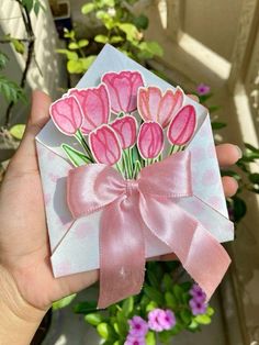 a hand holding a card with pink flowers on it and a ribbon around the front