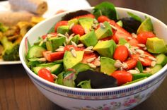 a salad with avocado, tomatoes, cucumbers and almonds in a bowl