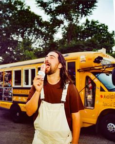 a man eating something in front of a yellow school bus with trees in the background