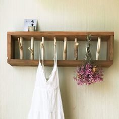 two white dresses hanging on a wooden shelf next to a vase with flowers in it