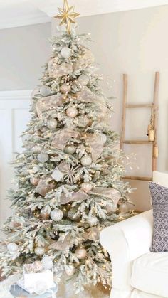 a white christmas tree with silver and gold ornaments on it in a living room area