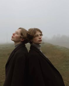 two people standing in front of a foggy field with their backs to each other