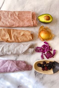 an assortment of fruits and vegetables laid out on a marble counter top with paper wrapping around them