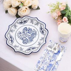 a white table topped with blue and white plates covered in floral designs next to flowers