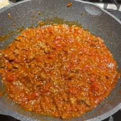 a pan filled with meat and tomato sauce on top of a stove burner next to a spatula