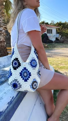 a woman sitting on top of a wooden bench holding a white and blue handbag