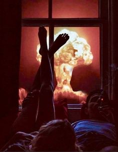 a person laying in bed with their feet up on the window sill and an image of a nuclear explosion behind them