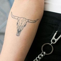 a woman with a tattoo on her arm holding onto a keychain that has a cow skull on it