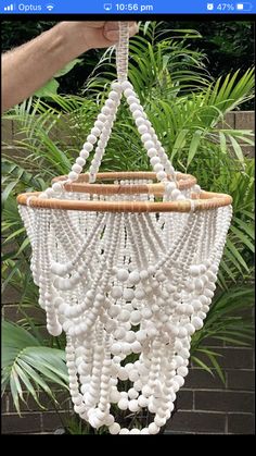 a person holding up a white beaded chandelier in front of some plants