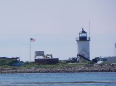 a light house sitting on top of a lush green hillside next to the ocean with an american flag flying in the background