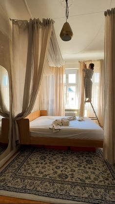 a person standing on top of a bed in a room with curtains hanging from the ceiling