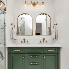 a bathroom vanity with two mirrors above it and green cabinetry, along with marble counter tops