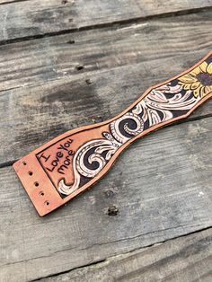 a leather belt with an ornate design on the front and back, sitting on a wooden surface