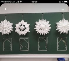 paper snowflakes are hanging on a green board