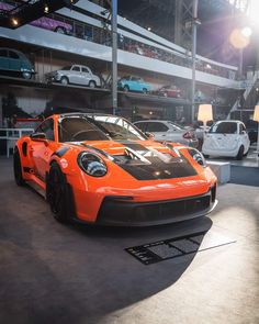 an orange sports car is parked in a showroom next to other cars on display