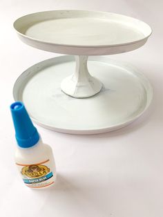 a white cake stand with a blue bottle next to it on a white table top