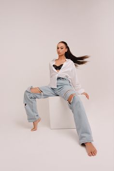 a woman sitting on top of a white box with her hair in the air and wearing ripped jeans