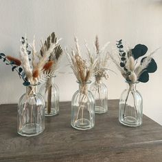 three glass vases with dried flowers and feathers in them