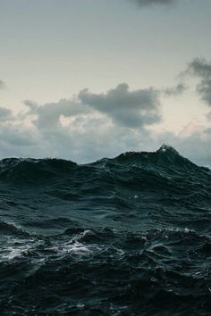 the ocean is very choppy and dark with some clouds in the sky above it