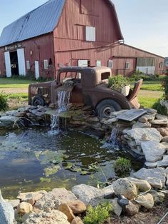 an old truck that is sitting in the grass next to a body of water and rocks