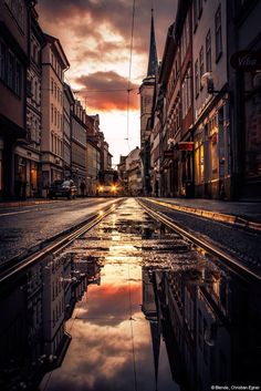 an empty street with buildings on both sides and water reflecting in the wet pavement at sunset