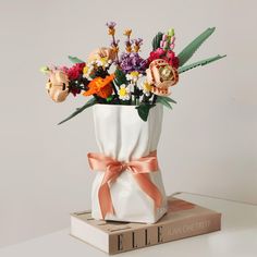 a white vase filled with colorful flowers on top of a book