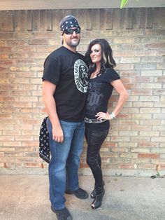 a man and woman standing next to each other in front of a brick wall wearing bandanas