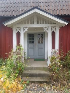 a red and white house with a blue door in front of some bushes on the ground