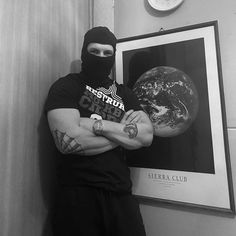 a man with his arms crossed standing in front of a poster and wearing a mask