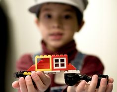 a young boy holding a toy truck with a house built out of legos on it