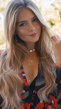 a woman with long blonde hair wearing a floral shirt and holding her hand to her ear