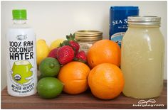 there are many different types of fruit on the counter top, including oranges, lemons, strawberries and coconut water